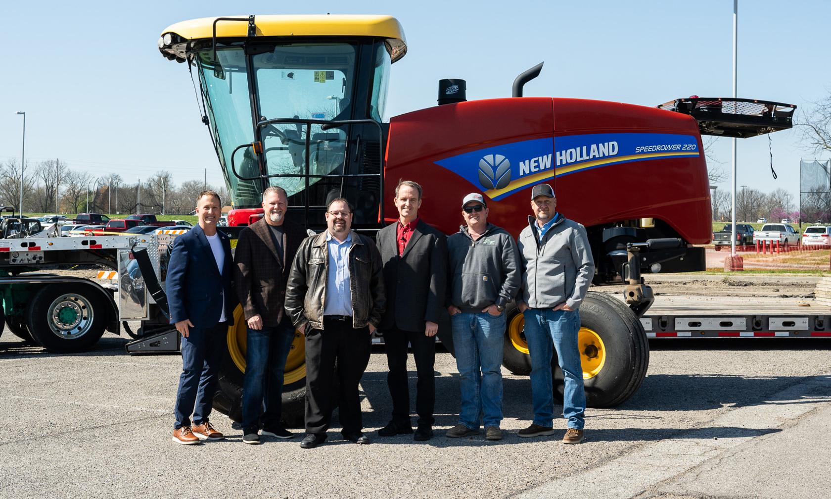 A large piece of farm equipment and a group of people standing in front of it