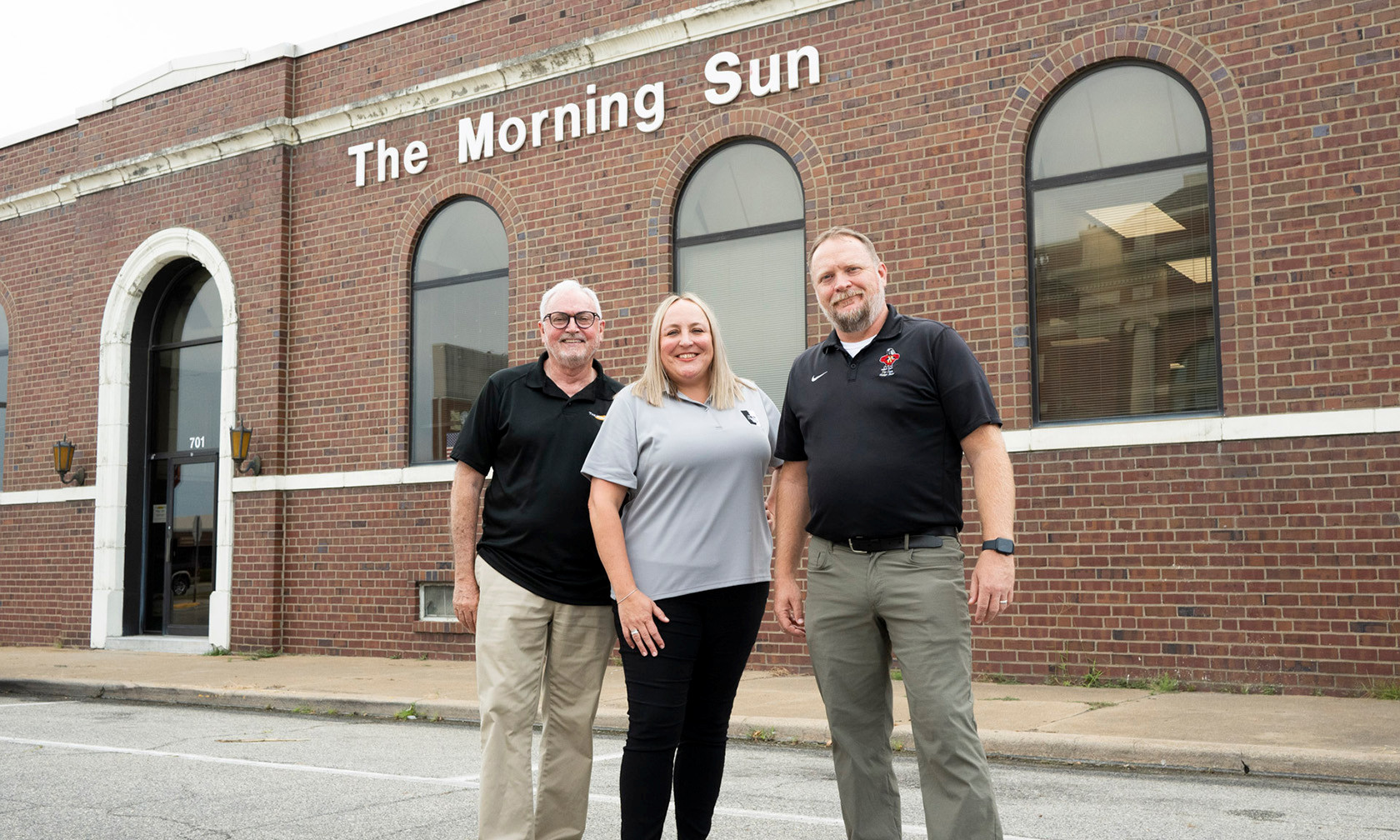 Three people standing outside newspaper office