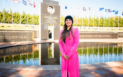 female veteran standing in front of a reflecting pool at a veterans memorial with flags in background