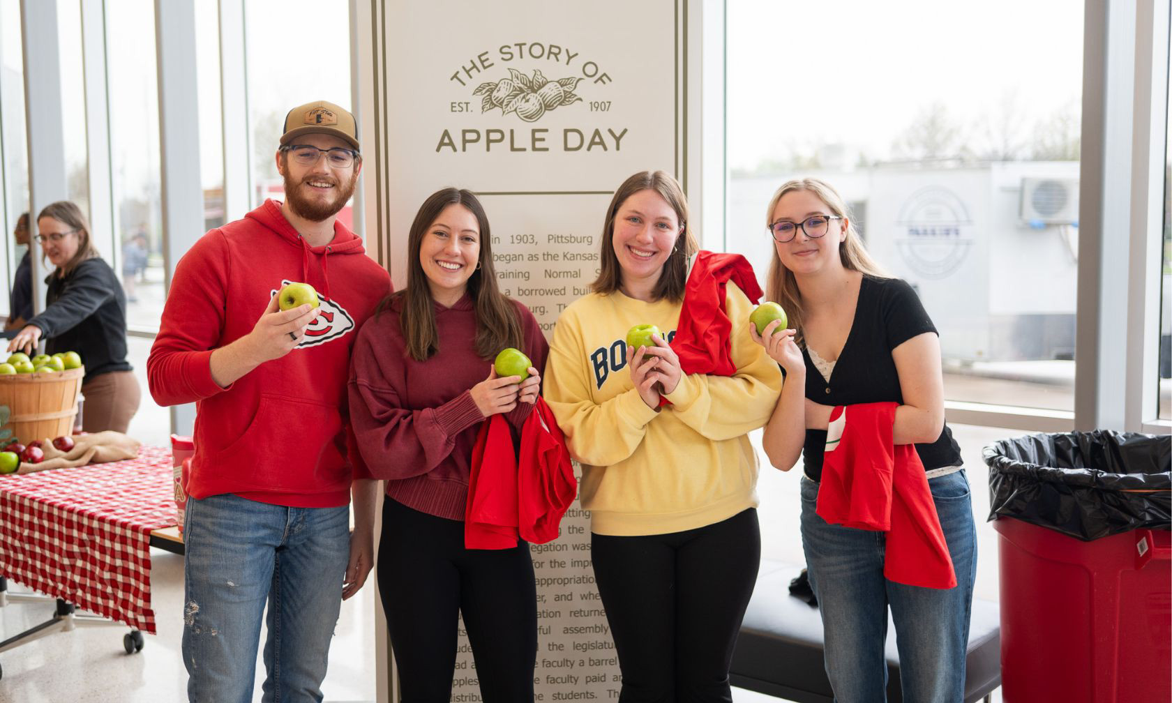 Students pose with apples in front of an apple day graphic at the Bicknell Center