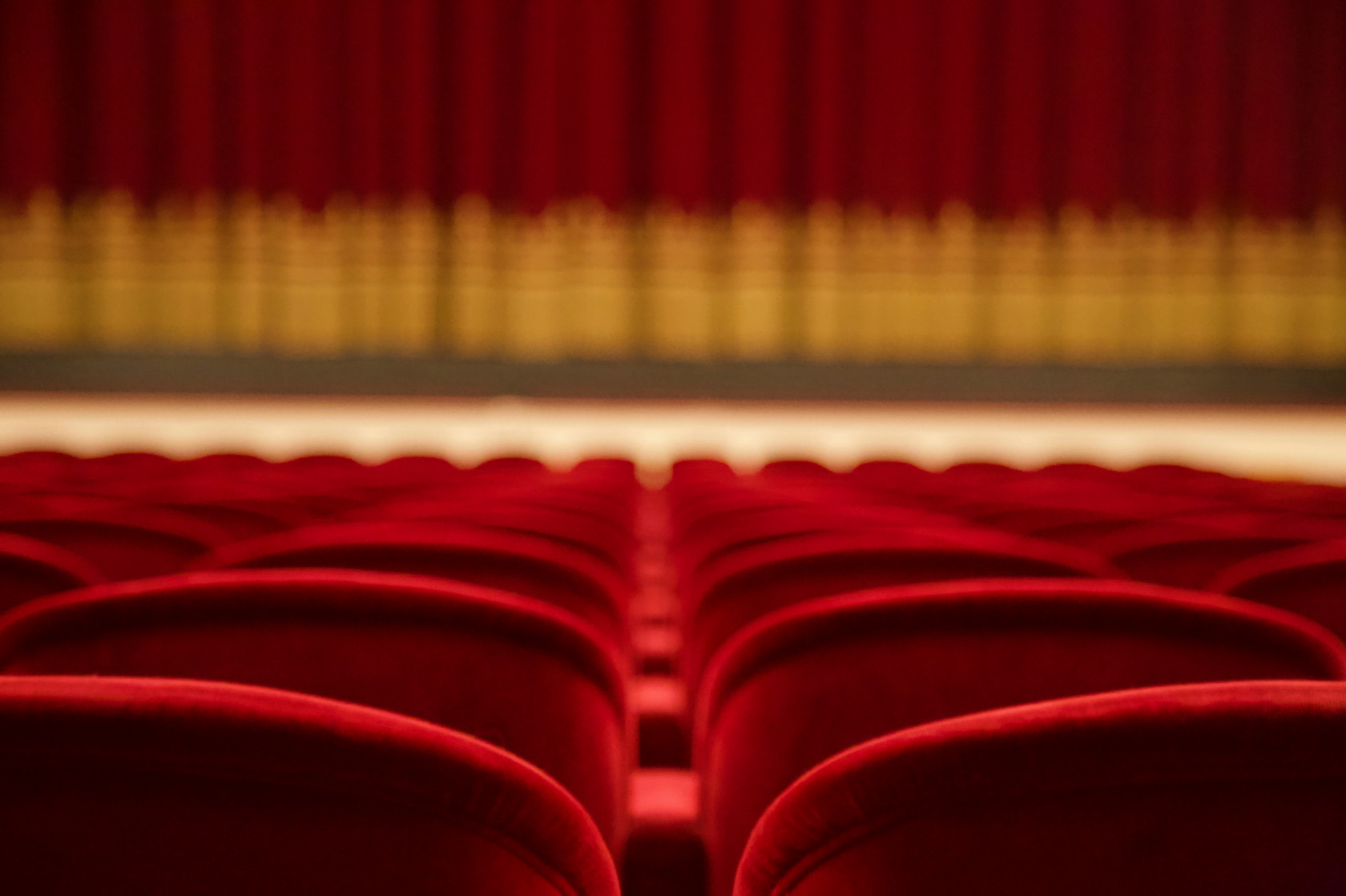 Generic backing to cushion red theatre seats facing a plush red velvet curtain stage