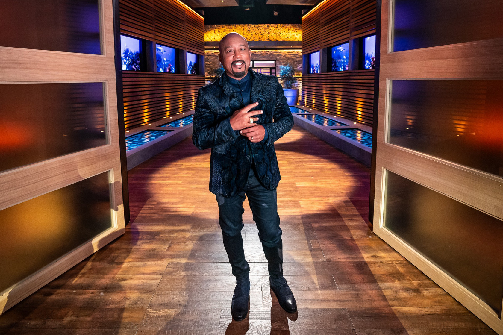 Daymond John stands, smiles, and poses on the set of Shark Tank