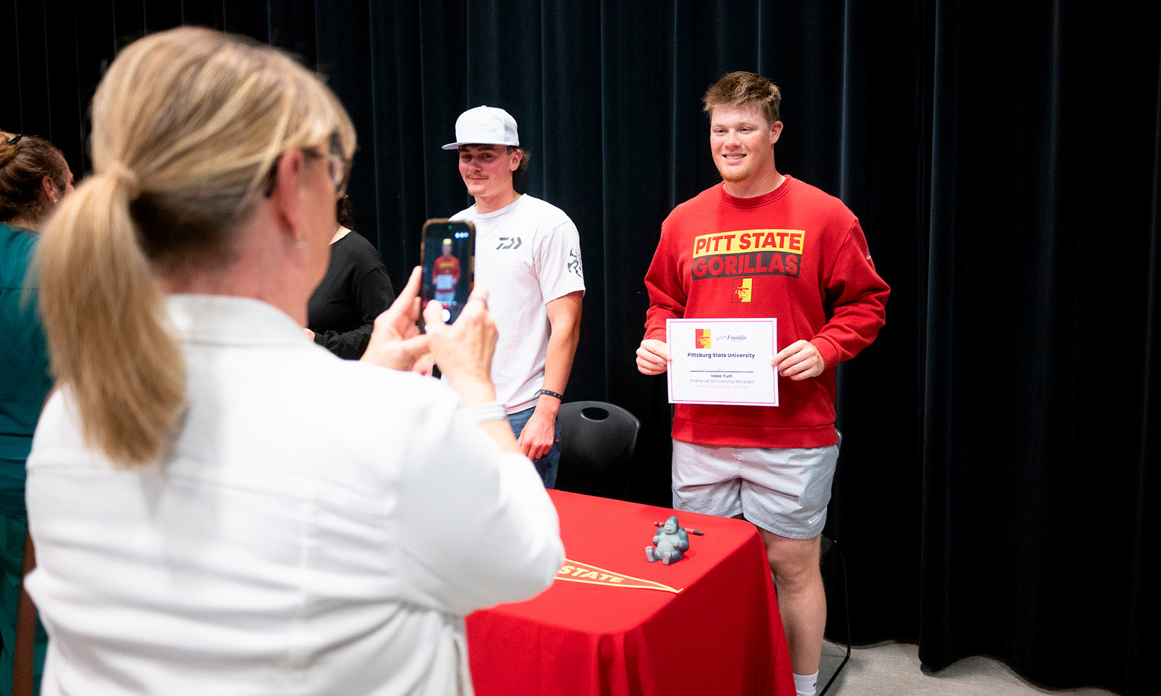 student smiling with certificate while mom snaps photo