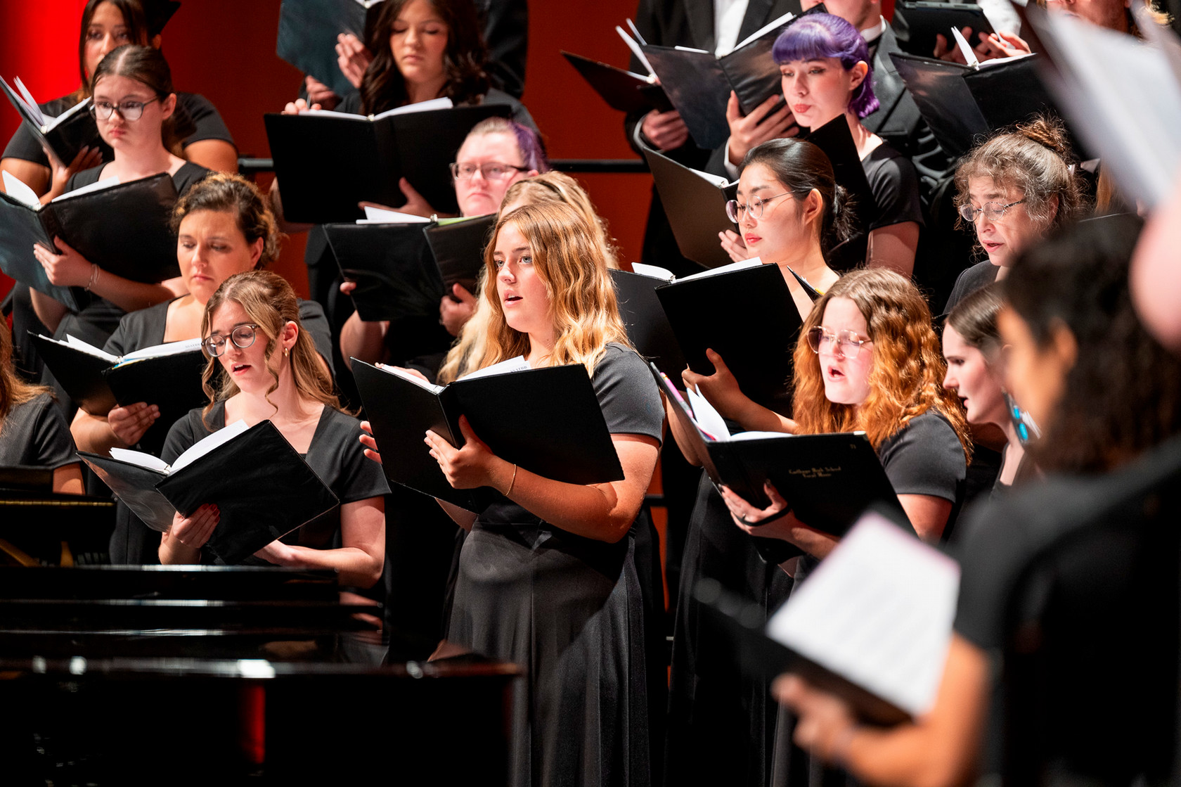 Students in choir dressed in black hold black choir binders and sing on risers on stage at the Bicknell Center