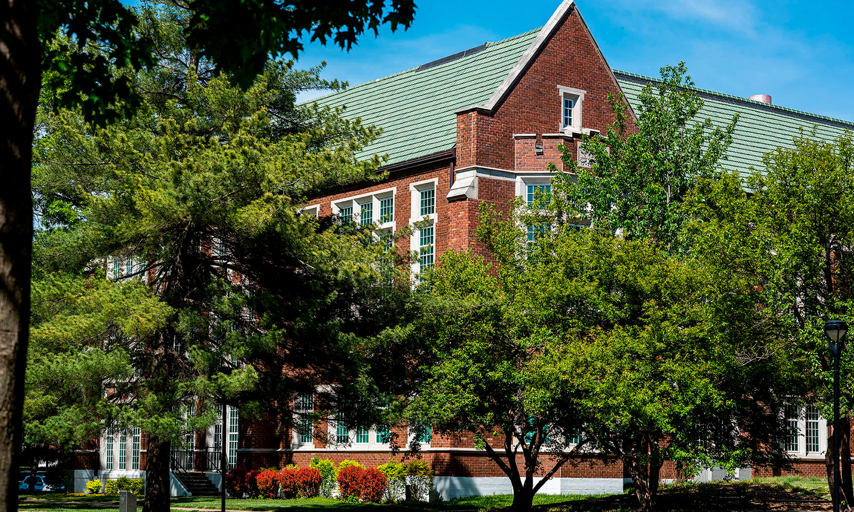 Porter Hall, home to the art department. A red brick campus building with green roof partially framed by leafy trees on a sunny day