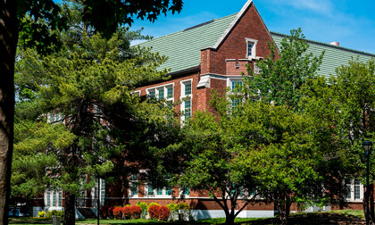 Porter Hall, home to the art department. A red brick campus building with green roof partially framed by leafy trees on a sunny day