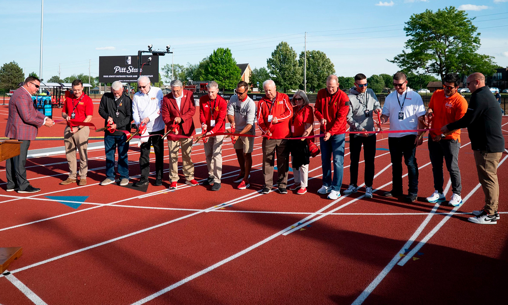 A dedication ceremony on a new track with several people holding scissors and a long red ribbon