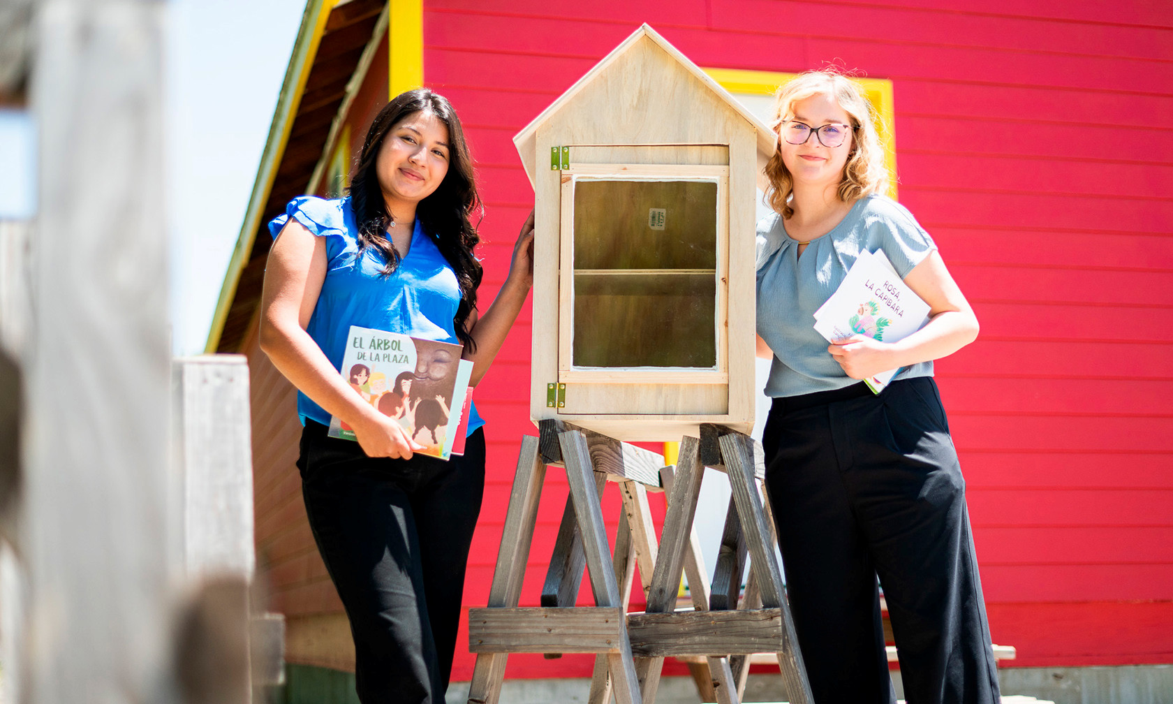 Students on the left and right of the unpainted little library pose with their creation, holding books as well. 