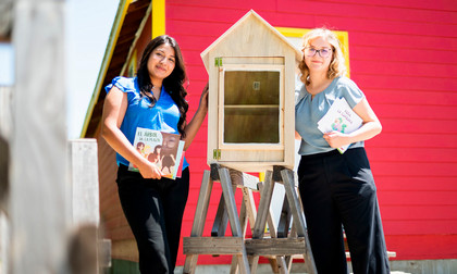 Students on the left and right of the unpainted little library pose with their creation, holding books as well. 
