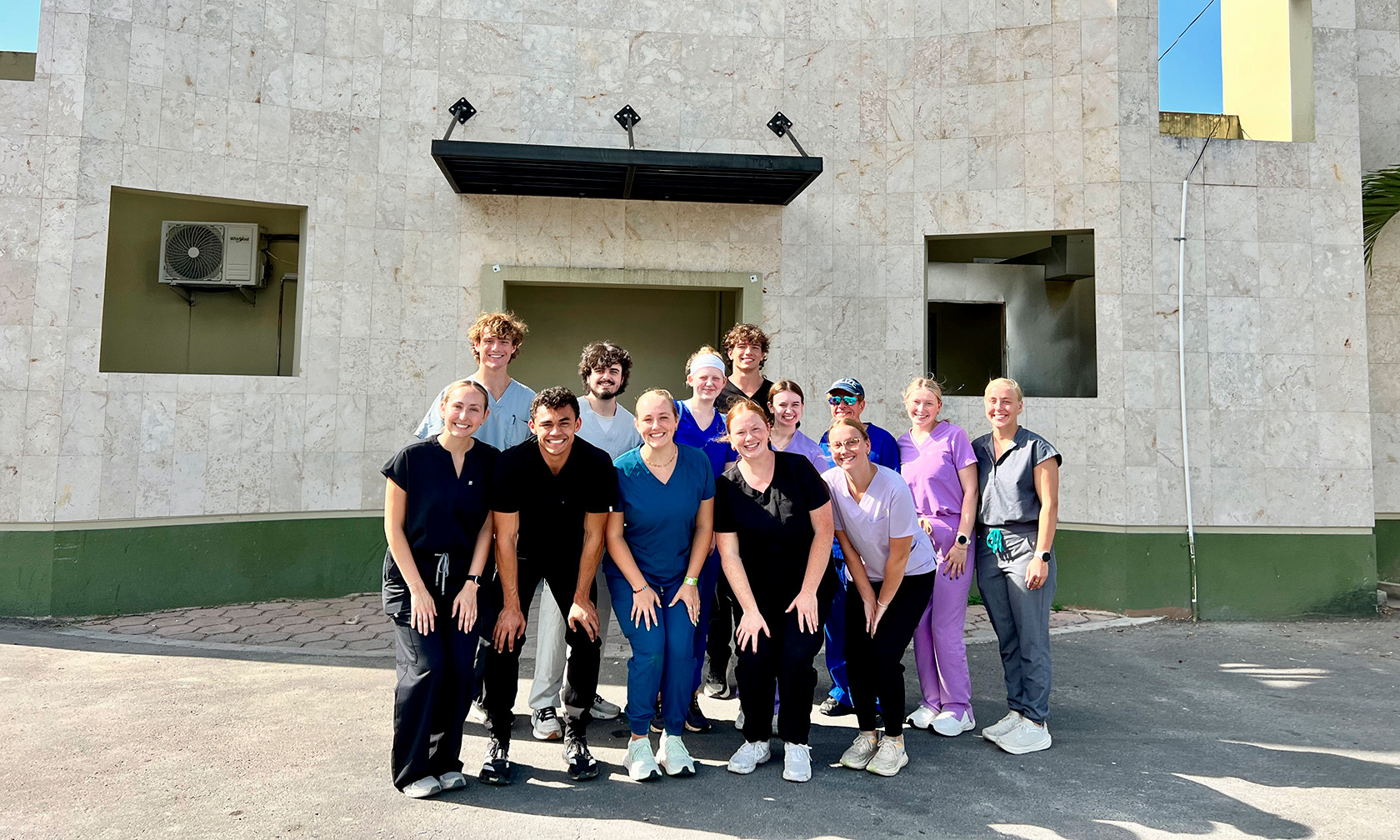 a group of college students posing in medical scrubs in front of a hospital in Belize