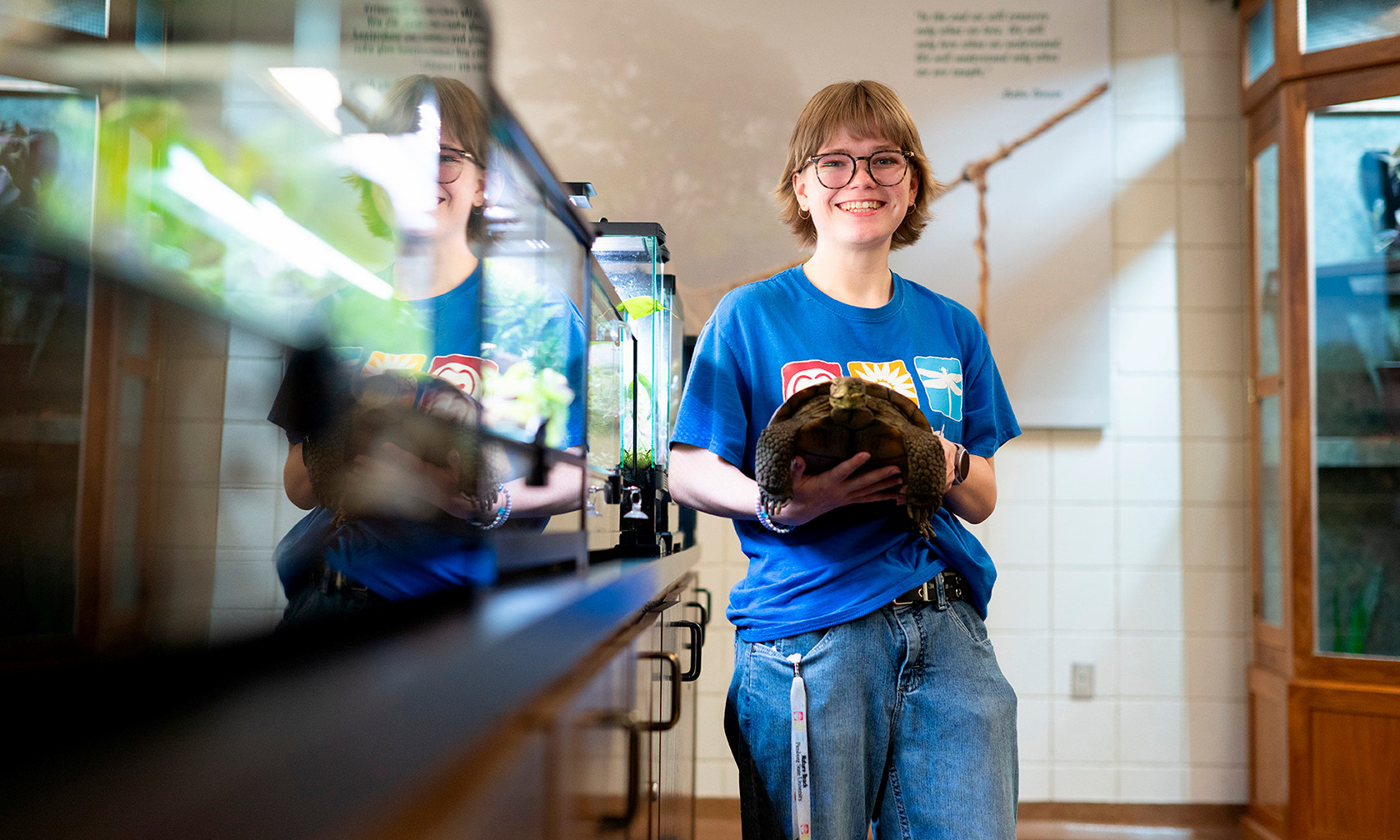 college student standing in science lab holding a tortoise, smiling