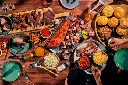 On a brown table sits cutting boards pilled with different bbq foods and sides