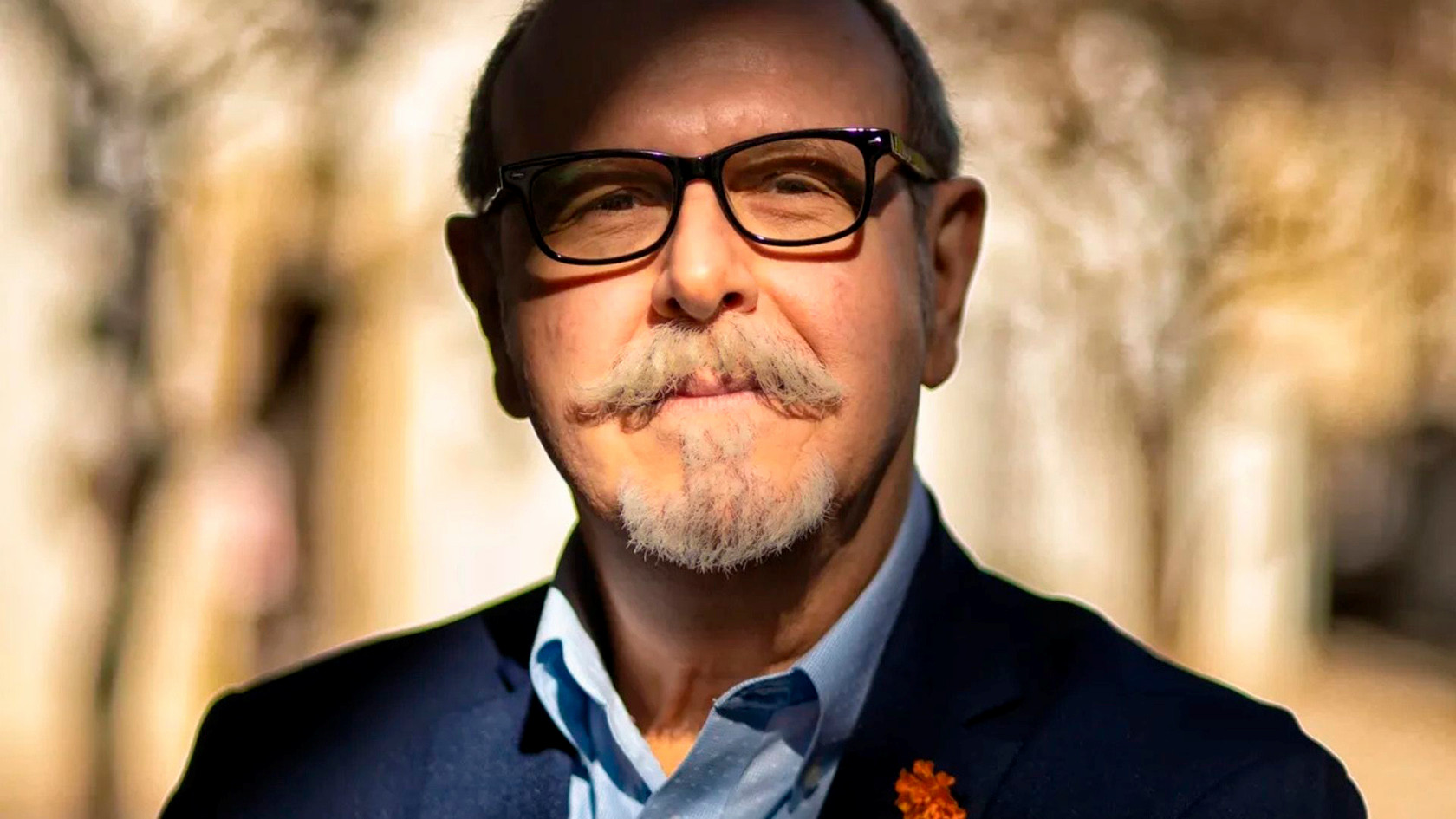A bald man from the shoulders up wearing black sunglasses and a curly mustache and goatee 