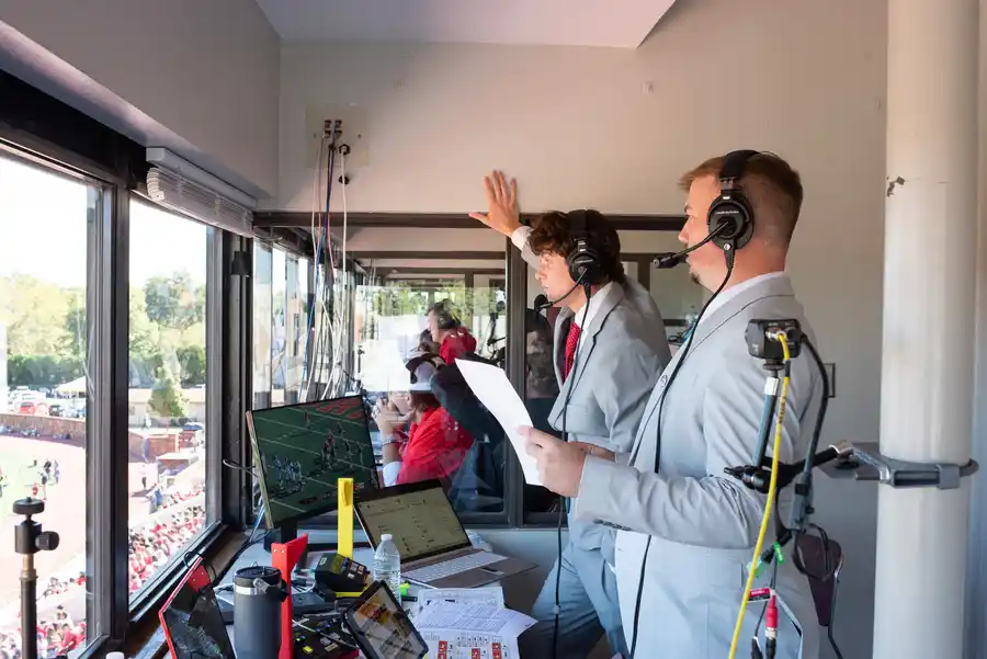 Two students announce the game from a press box in the stadium