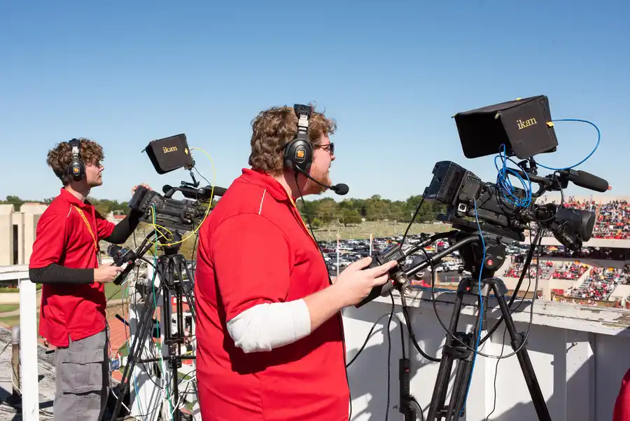 students use cameras to record the football game on top of the stadium