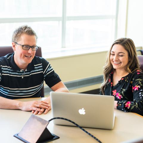 Professor and college student reviewing psychology coursework on laptop