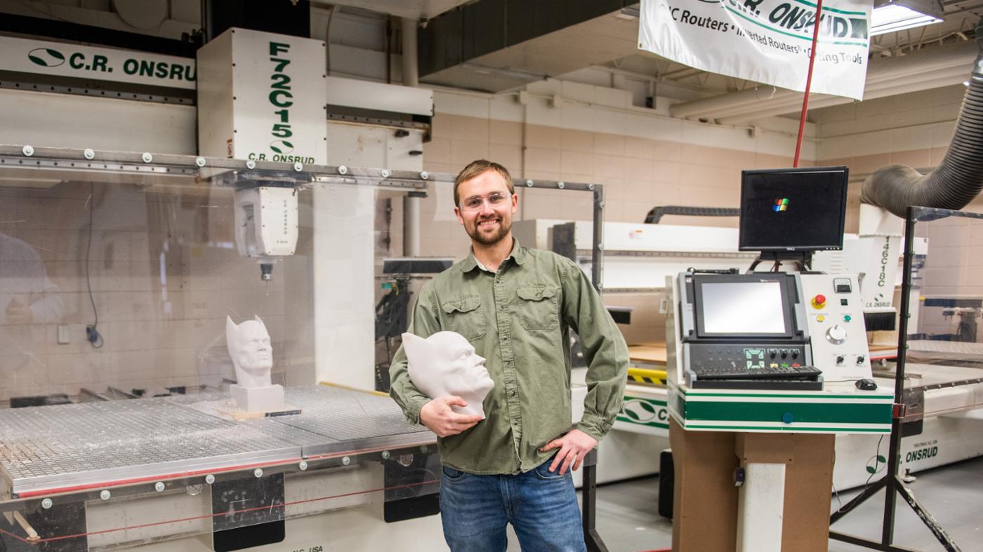wood student standing with product and wood processing machine in the background